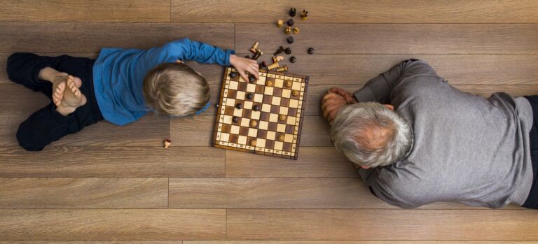 Isoisä ja poika lattialla pelaamassa shakkia