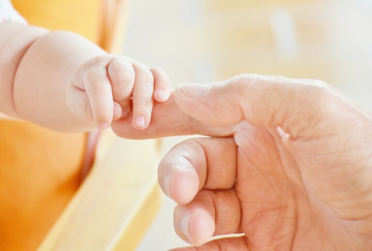 Kuvassa Vauvan käsi puristaa aikuisen sormea.