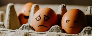 Kananmunapaketti, jossa kolme ruskeaa kananmunaa, joille piirretty ilmeet: iloinen, surullinen, arvosteleva
